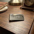 Metallic money clip with 'JPR' engraving on a wooden surface.