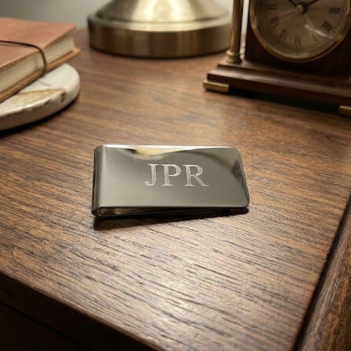 Metallic money clip with 'JPR' engraving on a wooden surface.