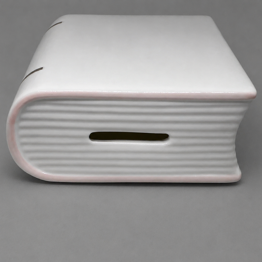 Coin slot on top of white porcelain baby bank.