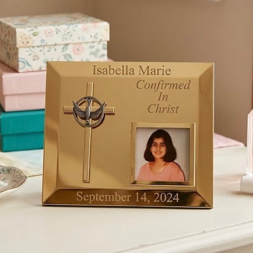 Gold photo frame for Confirmation with engraved text and a portrait, placed on a surface with decorative boxes and items.