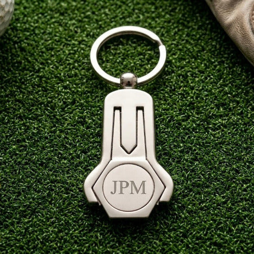 Silver keychain with 'JPM' initials on a green surface