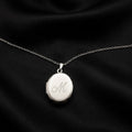 Silver locket with engraved 'M' on a black fabric background