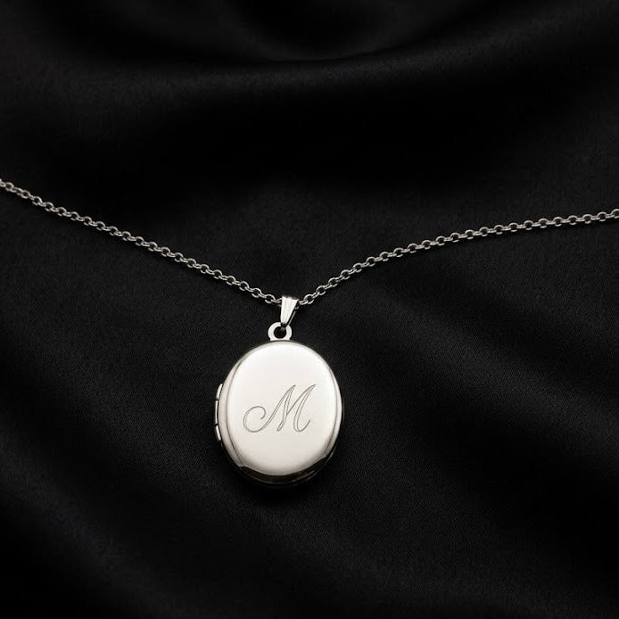 Silver locket with engraved 'M' on a black fabric background