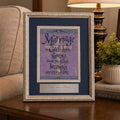 A framed scripture print reading 'Marriage is God's plan, strengthening one another' in purple and cream lettering, displayed on a wooden side table in a living room setting next to a lamp, a potted plant, and a sofa.