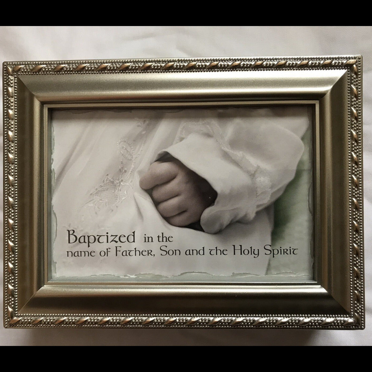 Framed photo of a baby's hand with religious text on a soft background on the cover of a music box.